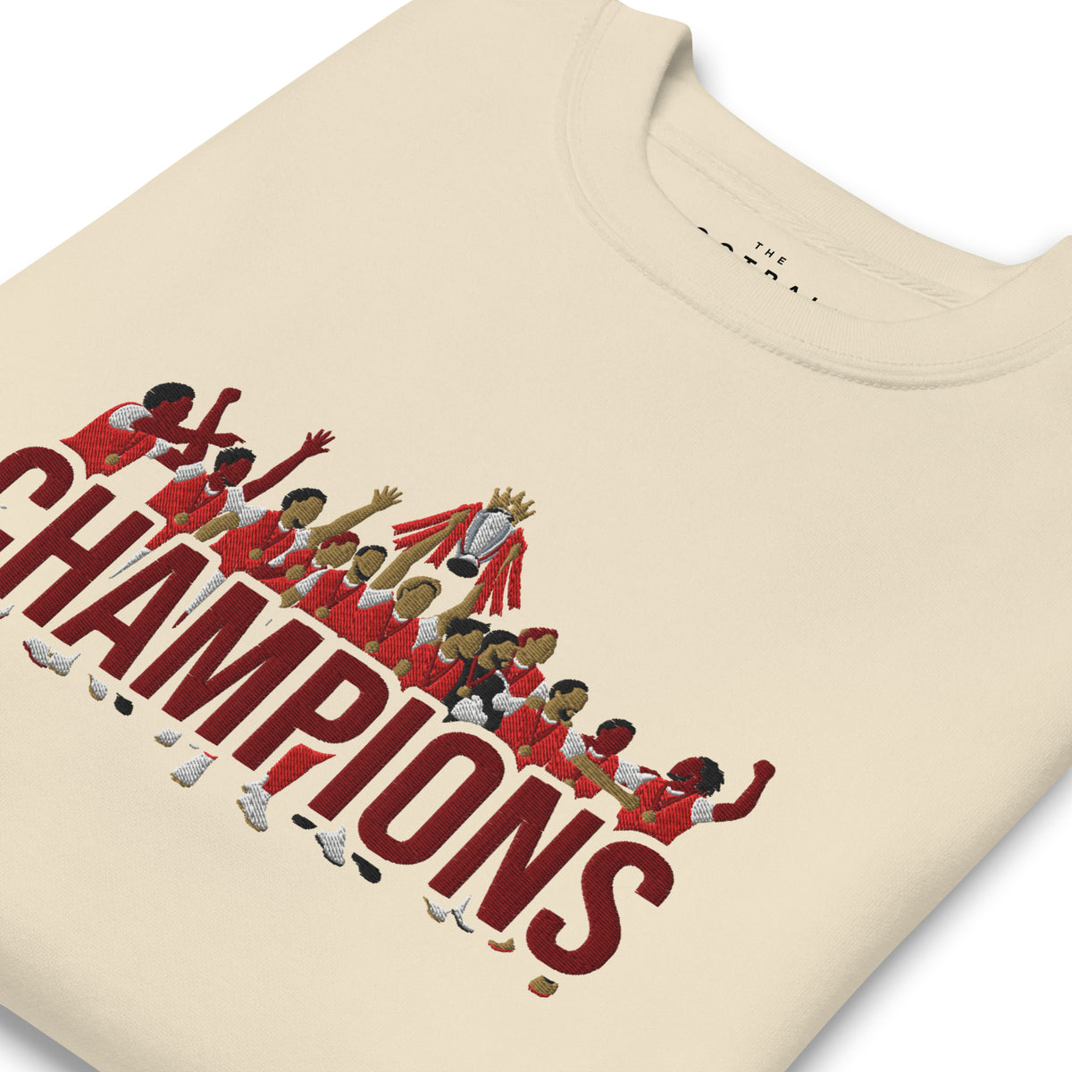 Folded angled view of Arsenal-inspired bone sweatshirt with trophy-lift embroidery and CHAMPIONS lettering